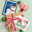 A framed print of Frosty the Snowman and a brown-paper-wrapped gift featuring a tag that says “It must be magic” with a picture of Frosty, surrounded by red and green ornaments.