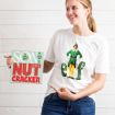 A smiling woman wears a white t-shirt featuring Buddy the Elf and holds a sign that reads “Son of a Nutcracker.”