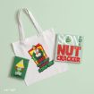 A white tote bag featuring an image of Buddy the Elf, accompanied by two square signs that read “Raised by Elves” and “Son of a Nutcracker.”