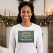 A smiling woman wearing a white long-sleeve shirt with a “Griswold’s Family Christmas” graphic showing a car carrying a tree.