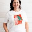 A woman wearing a white t-shirt featuring a Christmas Story graphic of Ralphie in a pink bunny suit, a Christmas tree, and the text “He looks like a deranged Easter bunny.”