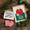 Two A Christmas Story-themed framed prints, one featuring a BB gun and one depicting the leg lamp, resting on a wooden surface with pine branches and ornaments.