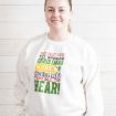 A smiling woman wears a white sweatshirt featuring the quote, “The best way to spread Christmas cheer is singing loud for all to hear,” with a small illustration of Buddy the Elf.