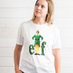A person wearing a white t-shirt featuring Buddy the Elf and the word “elf” in green glittery letters.