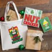 A white tote bag featuring Buddy the Elf, two wooden signs with movie quotes, and two gift-wrapped boxes on a wooden floor.