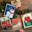 Four Christmas-themed prints featuring Frosty the Snowman, a nutcracker, a National Lampoon’s Christmas Vacation design, and a Leg Lamp, arranged on a wooden surface with pine branches, ornaments, and gifts.
