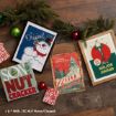 Framed art prints and ornaments themed after classic Christmas movies, arranged on a wooden floor with evergreen branches.