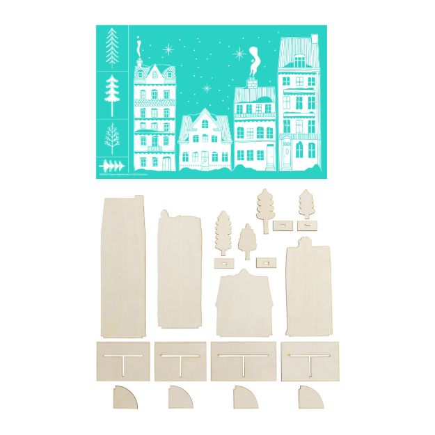 A turquoise screen printing stencil featuring a winter village scene above a collection of unpainted wooden cutout pieces for building the village houses and trees.