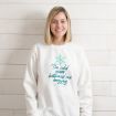 A woman smiling while wearing a white sweatshirt that features a light blue snowflake and the text “The cold never bothered me anyway. Just kidding, I’m freezing!”.