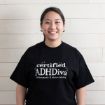 A smiling woman wearing a black t-shirt that says “certified ADHDiva” and “dramatic & distracted” in white text.