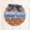 A round wooden wall sign featuring a blue ribbon at the top, white snowflakes, and the text “UP TO SNOW GOOD” in blue and white.