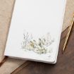 A white journal with a watercolor illustration of two sleeping rabbits, resting on a wooden surface next to a gold pen.